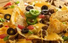 A close up of nachos with cheese, olives and jalapenos